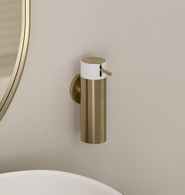 Dozownik mydła Ferro Smile w kolorze złotym z białym akcentem, zamontowany na ścianie nad białą umywalką, obok okrągłego lustra.